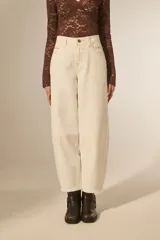 Pantalón jean color blanco, de corte barrel y tiro bajo, con detalles de tachas metálicas en los bolsillos delanteros y a lo largo de las costuras laterales.