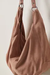 Bolso tipo hobo de gamuza negra, con forma holgada y cierre principal de cremallera. Se lleva al hombro con dos asas de correa delgadas sujetas con argollas metálicas plateadas.