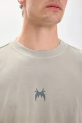 Remera verde de corte amplio y recto, con estampado en el centro de la espalda que incluye el texto "Live Concert" y una lista de géneros musicales.