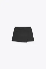 Falda pantalón corta color gris oscuro, de tiro medio y cintura asimétrica cruzada. Presenta bolsillos de vivo en delantero y cierre lateral con cremallera oculta en costura.