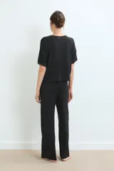 Conjunto de pijama negro, compuesto por una remera de manga corta con detalle de encaje en los puños y un pantalón largo de corte recto.