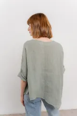 Blusa color naranja confeccionada en 100% lino, con escote en V, mangas cortas con vuelta y silueta amplia. Presenta terminación asimétrica y fila de botones decorativos en uno de los hombros.