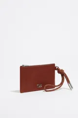 Monedero negro de piel con estructura blanda, asa de mano de cordón extraíble, logo metálico, acabados metálicos plateados, bolsillo interior y cierre con cremallera. Interior con etiqueta de tejido BIMBA Y LOLA.