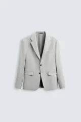Blazer gris claro de corte recto, confeccionado en tejido con viscosa. Tiene cuello con solapas de muesca, manga larga con puño abotonado, bolsillo de vivo en el pecho y bolsillos de parche en la cadera. El bajo tiene aberturas en la espalda y el cierre es con botonadura frontal.