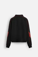 Chaqueta negra con detalles en rojo, cuello alto, cierre frontal con cremallera, bolsillos laterales y puños elásticos.