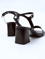 Sandalias de cuero charol negro con tira delgada sobre los dedos, pulsera con hebilla al tobillo y tacón cuadrado.