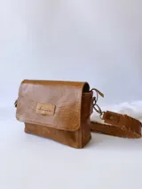 Bandolera color camel de cuero con forro de tela, correa corta con tientos y bolsillo interno.
