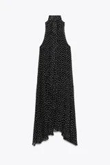 Vestido midi negro con estampado de lunares blancos, cuello halter con pañuelo integrado, sin mangas y bajo asimétrico. Cierre con abertura y botón en la nuca.