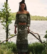 Pollera larga (midi/maxi) de tejido piqué, color verde oscuro con estampado en blanco/beige de motivos tropicales y palmeras. Presenta un diseño con fruncido en la parte inferior.