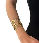 Pulsera ancha de bronce con diseño de círculos enlazados. Es ajustable para usar en la muñeca o en el antebrazo.