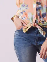 Blusa de gasa estampada a rayas verticales en tonos celeste, lila, naranja y marrón. Tiene cuello a la base con escote en V y botones. Delantera con bolsillo aplicado. Largo de manga regulable con presilla y botón. Terminación anudada opcional.