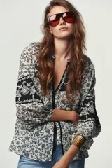 Blusa blanca con estampado floral en negro, cuello redondo con escote pico y manga larga abullonada. Presenta bordados y abalorios en el escote y los puños. Cierre frontal con botones.