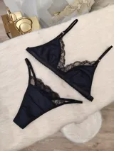 Conjunto de lencería negro, compuesto por un corpiño triangular de algodón con detalles de encaje y una tanga de algodón con detalles de encaje.