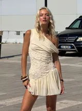 Vestido corto color crema, con escote asimétrico, detalle de bordado floral en el torso y falda con volados.