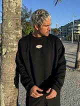 Buzo negro oversize con cuello redondo y logo ovalado bordado en el pecho.