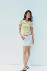 Camiseta blanca de corte slim fit, cuello redondo y manga corta con acabados en puntilla. Tiene detalle de frunces en los laterales y tejido combinado a contraste efecto doble en cuello, mangas y ruedo.