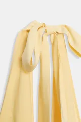 Vestido midi de tejido fluido color amarillo pálido, con cuello halter que se anuda en la parte superior y escote pronunciado en pico.