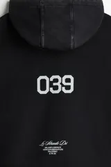 Sudadera tipo canguro de algodón pesado con efecto lavado oscuro, corte oversized y hombros caídos. Presenta estampado frontal en blanco con texto cursivo "Le Strade Di MMXXVI", dos banderas a cuadros, texto pequeño en la parte superior derecha y texto vertical en la manga izquierda. La manga derecha tiene un patrón de estrellas delineadas.