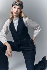 Chaleco sastrero de denim azul oscuro con elastano, acceso con botones con logo, falsos bolsillos ojal y tira de ajuste en la espalda con hebilla. Bordado de alas en la espalda.