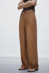 Pantalón de vestir color marrón claro, de tiro medio, corte ancho y con pliegues frontales.