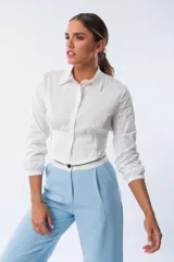 Camisa blanca de algodón y elastano, con corte cropped, cuello clásico, mangas largas con puños elásticos y cintura ajustada con elástico.