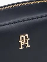 Cartera cruzada tipo cámara de poliuretano color azul marino, con cierre principal de cremallera y monograma TH metálico dorado al frente. La correa larga es ajustable y presenta la cinta distintiva de la marca en rojo, blanco y azul.