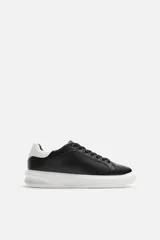 Zapatillas urbanas de cuero sintético negro con cordones y suela blanca de goma con volumen.
