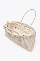 Bolso shopper alargado color beige con diseño trenzado, doble asa de hombro y cierre con botón imantado. Incluye bolsa interior con cierre fruncido.