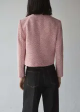 Chaqueta de tweed rosa con cuello redondo, cierre frontal con botones plateados, dos bolsillos de parche delanteros, corte entallado, forro interior y mangas largas.