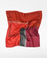 Pañuelo cuadrado de poliéster reciclado con estampado cartográfico en bloques de color naranja, rojo, bordó y gris. Presenta el logo de Adolfo Dominguez y detalles de texto inspirados en mapas.