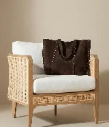 Bolso tipo tote de gamuza sintética color marrón chocolate, con doble asa de hombro y detalles de tachas metálicas plateadas. Amplio compartimento principal sin cierre.