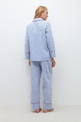 Conjunto de pijama celeste a rayas verticales blancas, compuesto por camisa de manga larga con cuello y pantalón largo de corte recto. Presenta vivos rojos en cuello, puños, ruedo de la camisa y ruedo del pantalón.