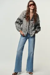 Blusa blanca con estampado floral en negro, cuello redondo con escote pico y manga larga abullonada. Presenta bordados y abalorios en el escote y los puños. Cierre frontal con botones.