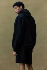 Campera con capucha negra, corte oversized, con cierre frontal, bolsillos y puños acanalados.
