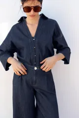 Camisa de denim azul con cuello de solapa, escote en pico, cierre frontal con botones y mangas anchas hasta el codo.
