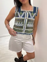 Chaleco corto de denim azul con bordado artesanal en tonos naranja, blanco y marrón. Tiene escote cuadrado, cierre de botones y terminaciones desflecadas.