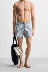 Bañador de hombre con rayas verticales azules y blancas, de corte medio, con cintura elástica ajustable con cordón, bolsillos laterales y trasero con solapa.