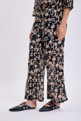 Pantalón de corte palazzo con estampado floral en tonos beige sobre fondo negro.