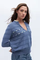 Sweater azul de punto con escote en V, detalles calados y lazo en el escote. Tiene ribetes con volados en contraste en el cuello y puños.