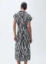 Vestido camisero midi con estampado de cebra en blanco y negro, cuello camisero, mangas cortas, cierre frontal con botones y lazo ajustable en la cintura.