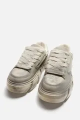 Zapatillas bajas color gris claro con cordones y suela gruesa con diseño irregular.