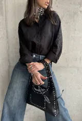 Camisa negra con bordados florales en las mangas, cuello clásico y cierre frontal con botones.