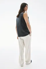 Pantalón de sarga color crudo con finas rayas verticales en gris, de tiro alto con cintura elástica y cierre decorativo. Tiene bolsillos laterales discretos y piernas anchas con pliegues cosidos adelante y pliegues planchados atrás.