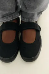 Zapato plano tipo bailarina en tejido color negro. Detalle de pespunte en el cuerpo, tira con adhesivo ajustable, suela engomada y acabado en punta redonda.