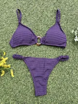 Conjunto de bikini color violeta confeccionado en tela texturada. El corpiño es de estilo top con una hebilla ovalada marrón en el centro y breteles finos. La bombacha es de corte colaless con detalle de frunces en los laterales.