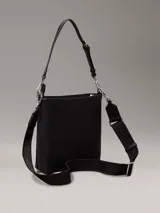 Cartera tipo saco pequeña Calvin Klein color negro, de cuero sintético granulado. Tiene dos correas desmontables: una correa fina ajustable y una correa ancha ajustable con logo jacquard.