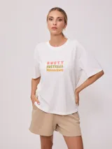 Remera negra de algodón con corte holgado y estampado frontal con el texto "Rusty Australia Mermaid Beach" en colores naranja, verde y amarillo.