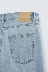 Jeans de denim de algodón, color negro lavado, con tiro medio, corte ajustado en cadera y muslos, y pierna que se estrecha hacia el tobillo. Presenta cinco bolsillos y cierre frontal con cremallera y botón.