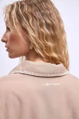 Cazadora color beige con bordados en hilo blanco en cuello, bolsillos y puños.