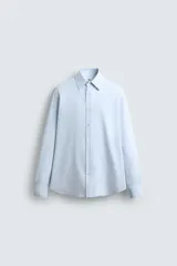 Camisa celeste de algodón con estructura twill, corte regular, cuello solapa, manga larga con puños abotonados y cierre frontal con botones.